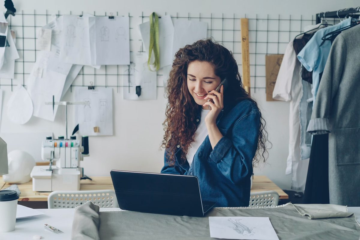 A clothing designer on a call at her workbench